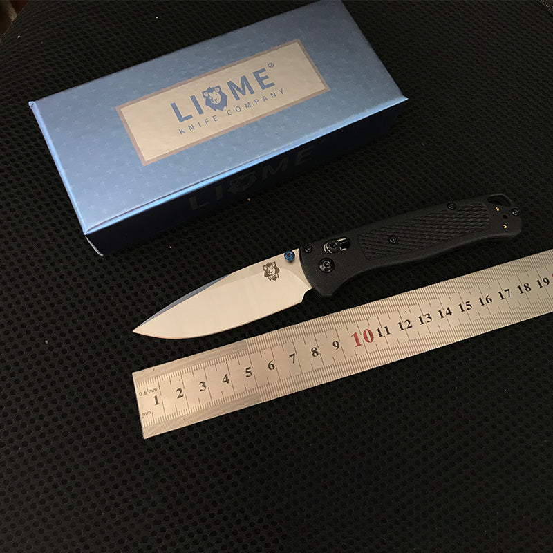 Black handled folding knife with silver blade laid beside a steel ruler showing about 19cm overall length
