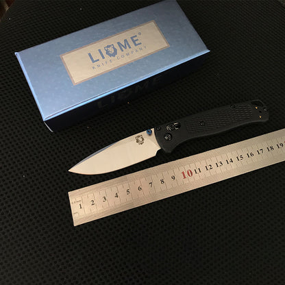 Black handled folding knife with silver blade laid beside a steel ruler showing about 19cm overall length