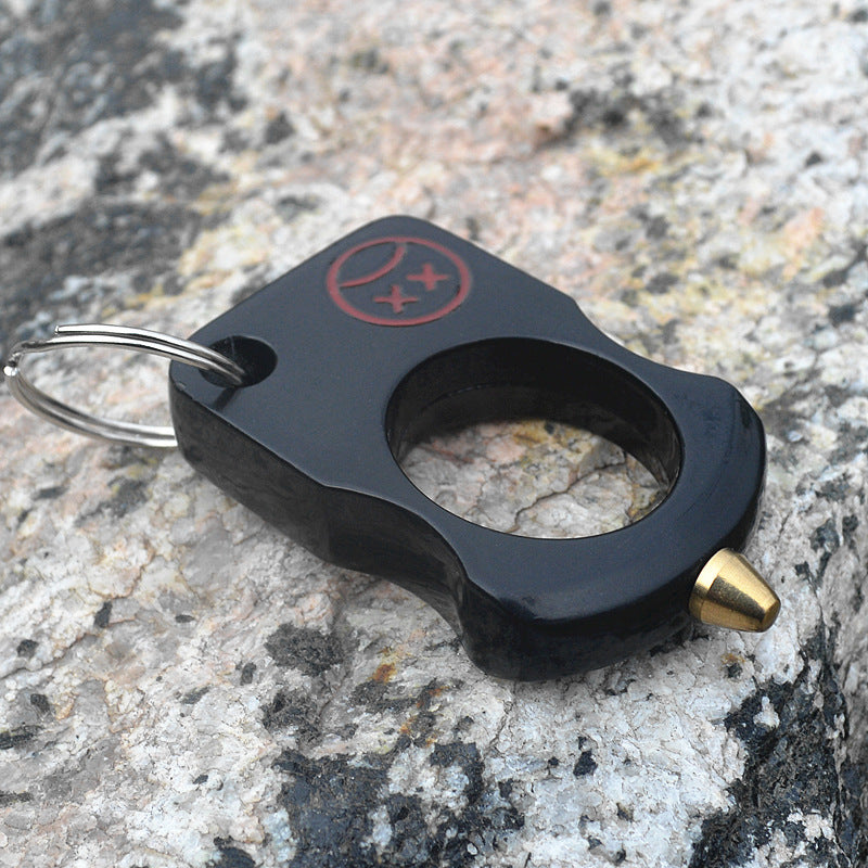 Black single-hole zinc alloy knuckle keychain with red cartoon print and brass cone tip resting on grey stone