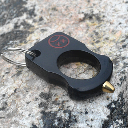 Black single-hole zinc alloy knuckle keychain with red cartoon print and brass cone tip resting on grey stone