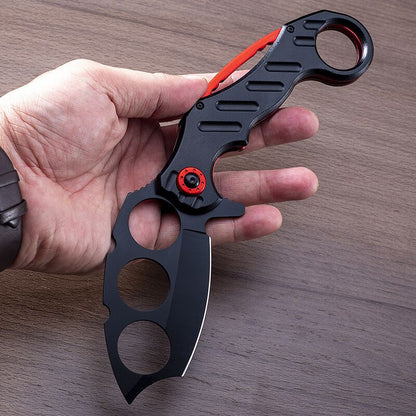 Black folding knuckle knife with red accents held in hand showing finger holes