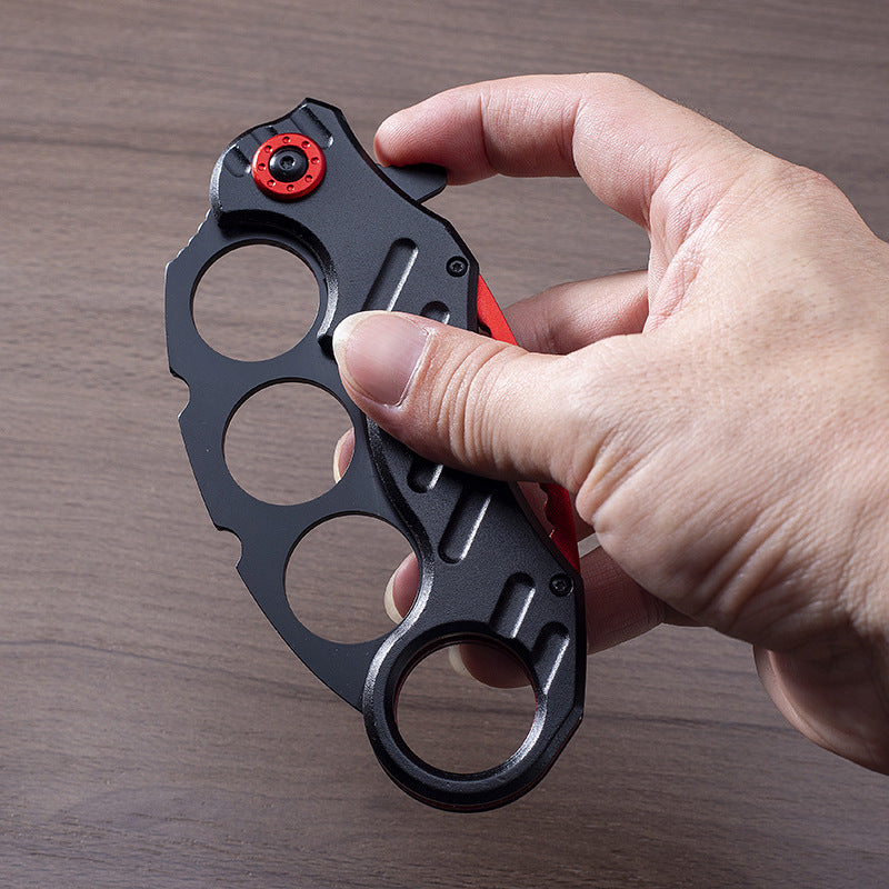 Black folding knuckle knife with red accents held showing ring grip texture