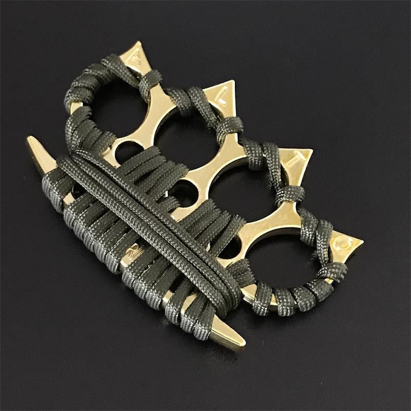 Black four-finger knuckle duster with umbrella cord wraps propped against a piece of wood in bright light