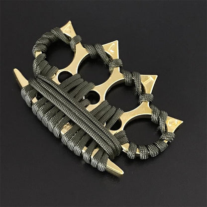 Black four-finger knuckle duster with umbrella cord wraps propped against a piece of wood in bright light