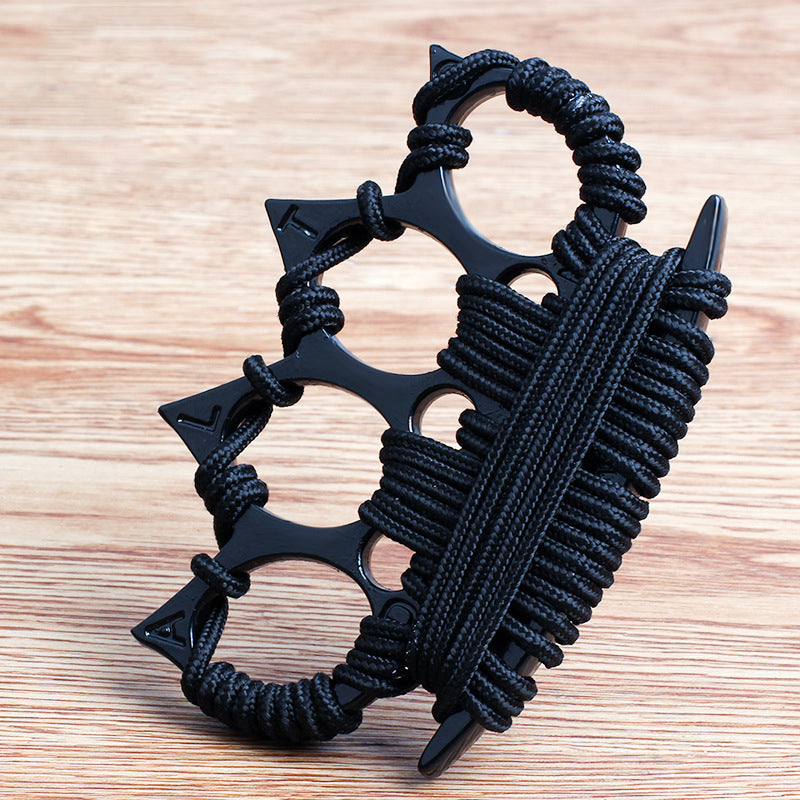 Black four-finger knuckle duster with black umbrella cord wraps and embossed points, standing on a wooden tabletop