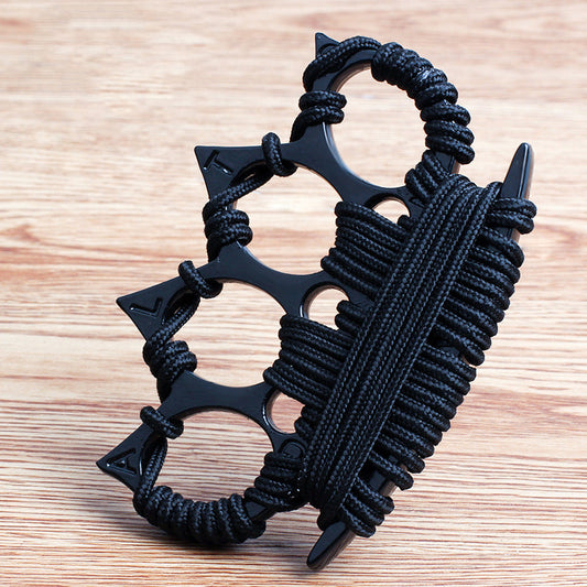 Black four-finger knuckle duster with black umbrella cord wraps and embossed points, standing on a wooden tabletop