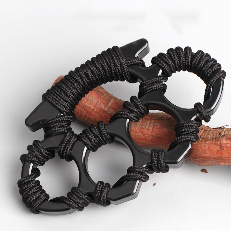 Black woven knuckle duster resting on a wooden branch showing the rope wrapping and four finger openings