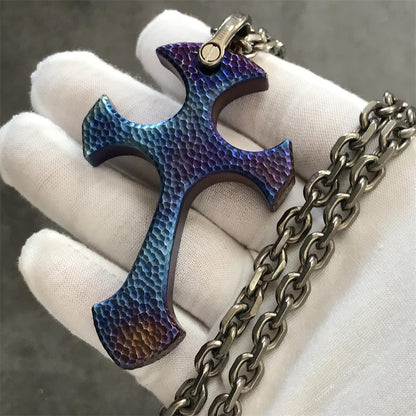 Blaze finish TC21 titanium cross pendant held in a white gloved hand showing blue purple hammered surface