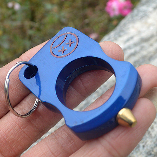 Blue anodized single-hole knuckle keychain worn on a finger outdoors, brass-toned cone tip and steel split ring visible