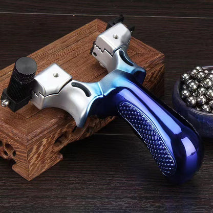 Blue slingshot with a silver fade resting on a carved wooden box, laser module mounted on one fork arm