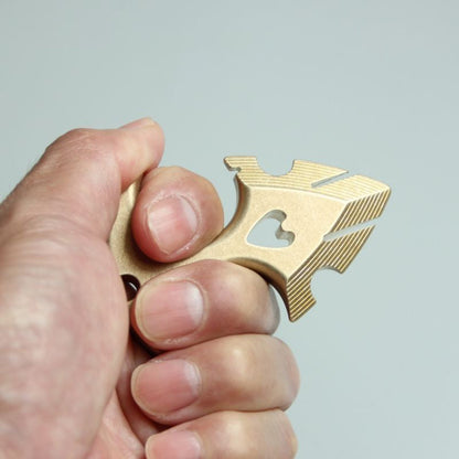 Hand gripping the brass anchor pendant in a closed fist, showing the ridged flukes and the thickness of the body.