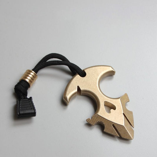 Brass anchor pendant on a light gray surface with a black paracord lanyard, brass bead and black cord lock attached.