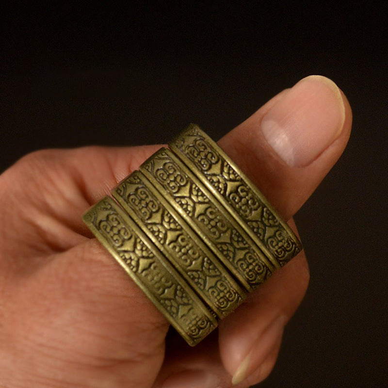 Close-up of brass hexagon bands stacked on one finger showing the engraved pattern on every band