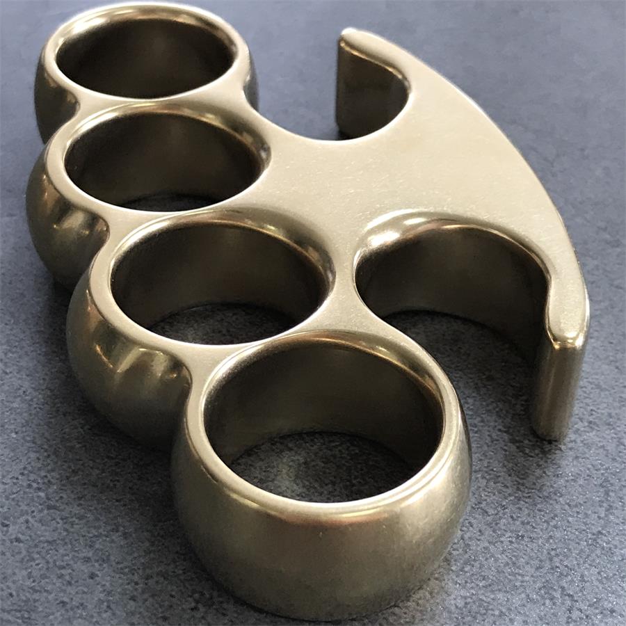 Angled close-up of the brass knuckle duster showing the talon tip and rounded finger-hole rims