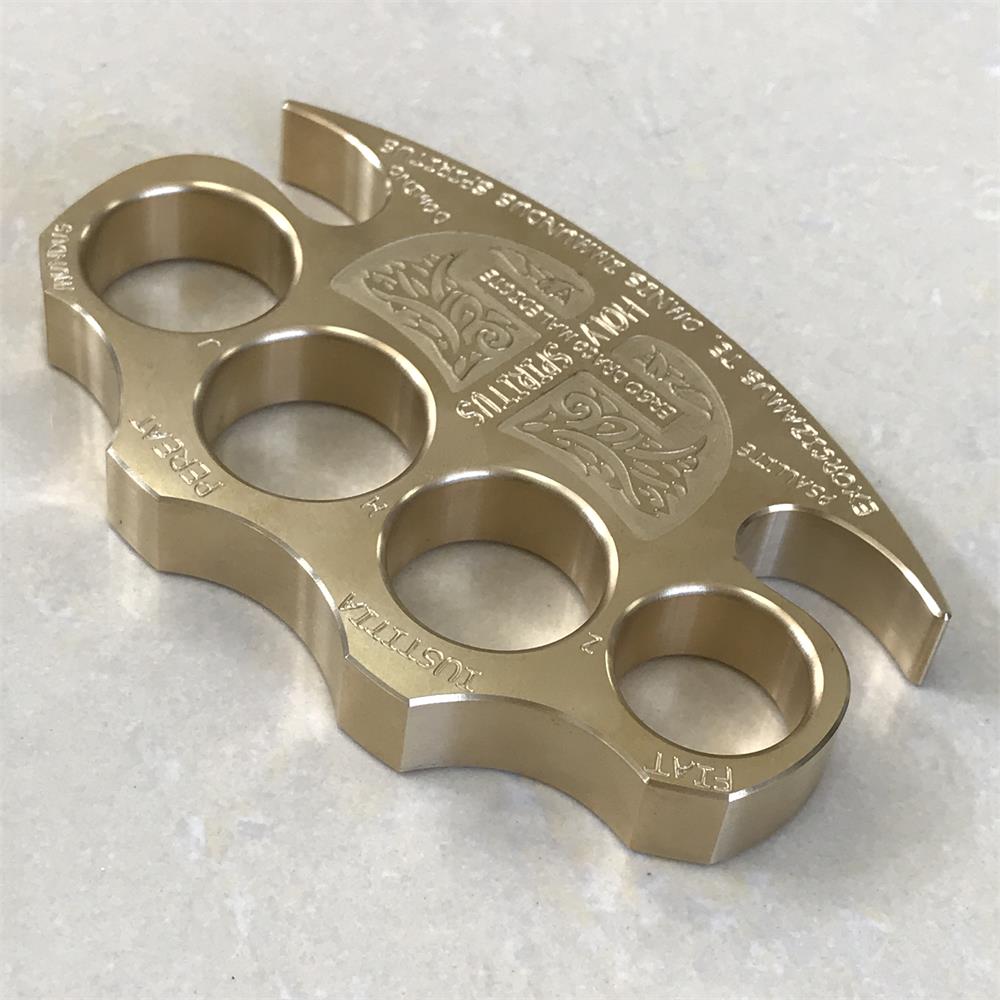 Brass knuckle duster with crest engraving resting on a light tiled floor, claw end toward the lower right