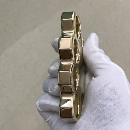 Close side view of a brass knuckle duster showing the squared ridge blocks between the finger holes