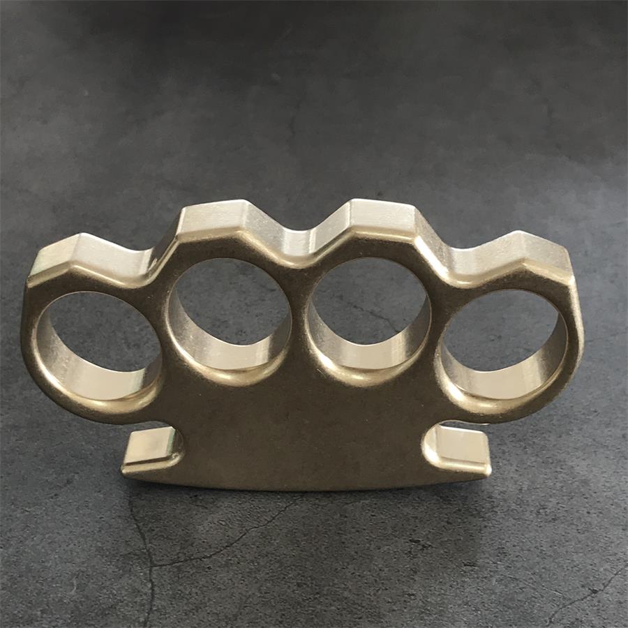 Front face of the stonewashed brass knuckle duster laid flat on a dark textured surface.