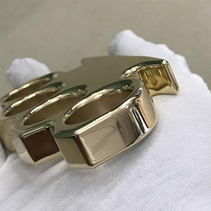 Brass knuckle duster lying flat on kraft paper with the four finger holes and top bar catching the light