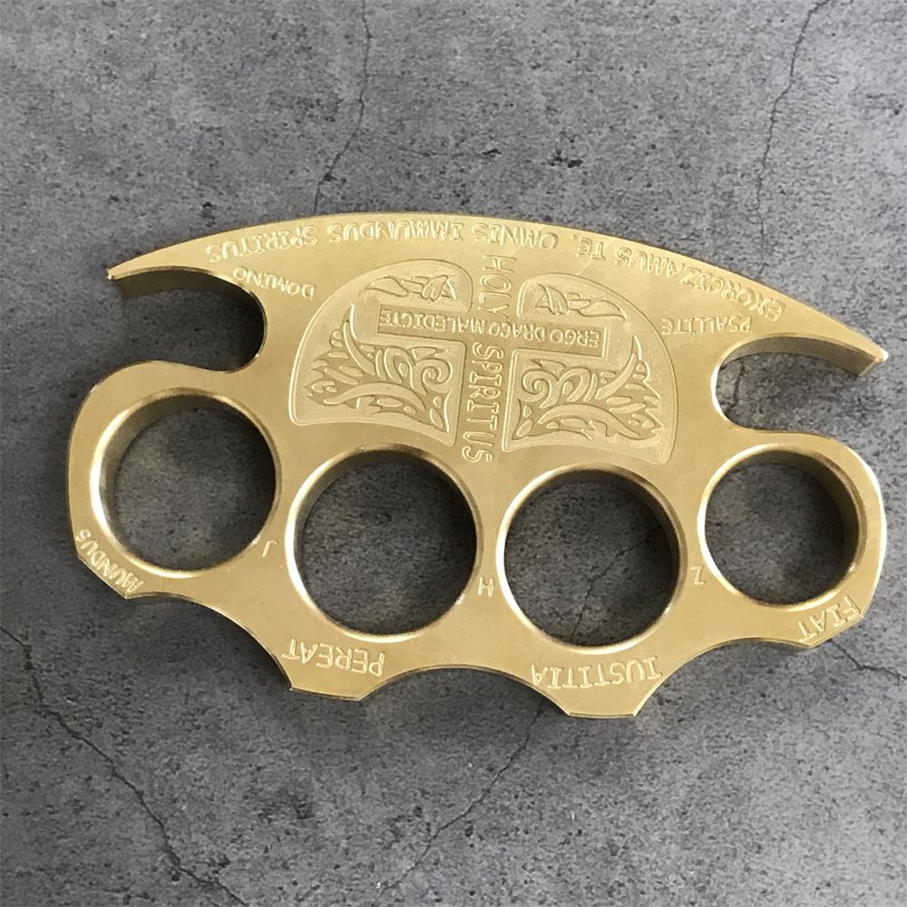 Front view of a brass knuckle duster lying flat on grey stone, four round finger holes under the arched top edge