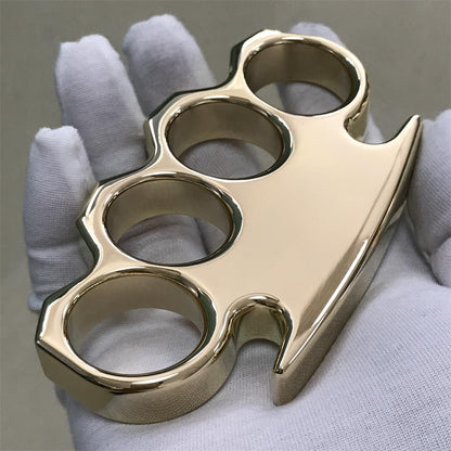 Solid brass knuckle duster with mirror polish held in a white gloved hand, front face and pointed end facing the camera