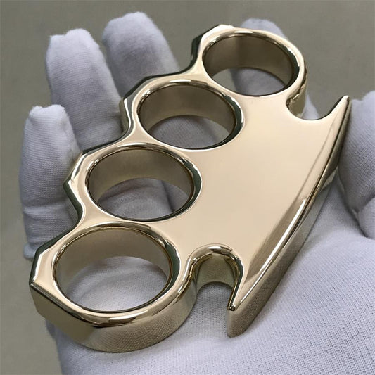 Solid brass knuckle duster with mirror polish held in a white gloved hand, front face and pointed end facing the camera