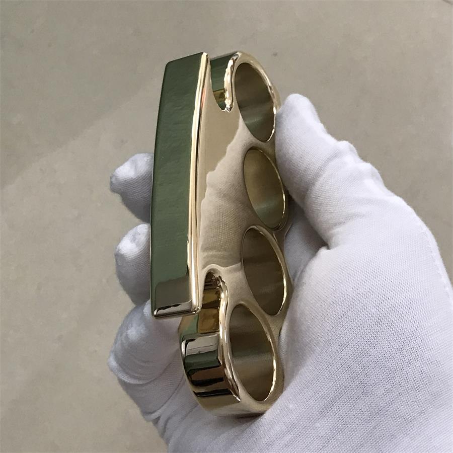 Brass knuckle duster held in a gloved hand showing the side profile of the finger holes