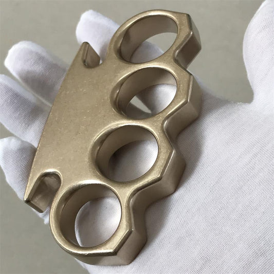 Reverse angle of the stonewashed brass knuckle duster in a gloved hand, highlighting the contoured palm side.