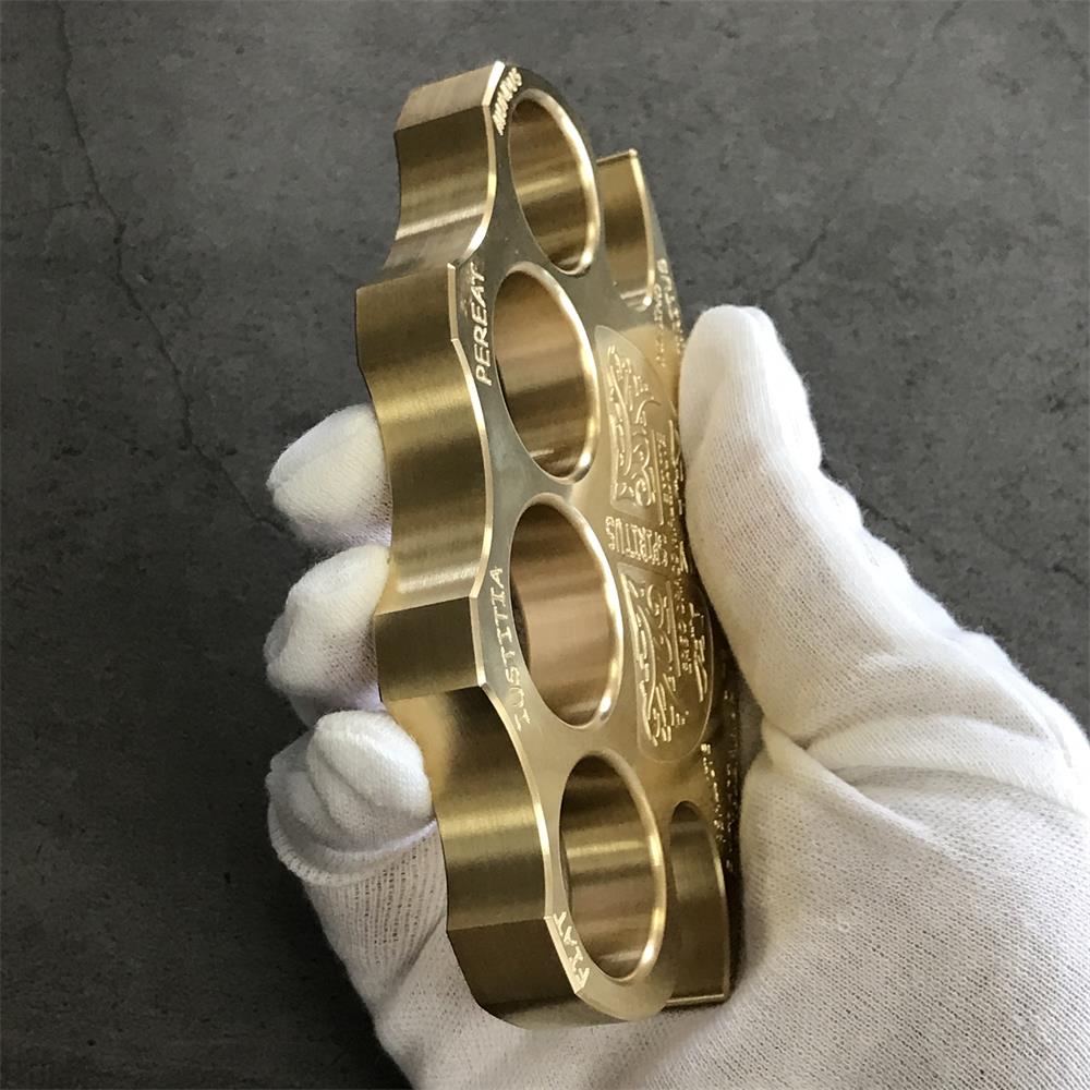 Side view of a brass knuckle duster held in a white gloved hand showing the satin walls and round hole rims