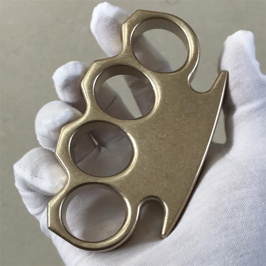 Side profile of the brass knuckle duster held in a gloved hand, showing its solid thickness.