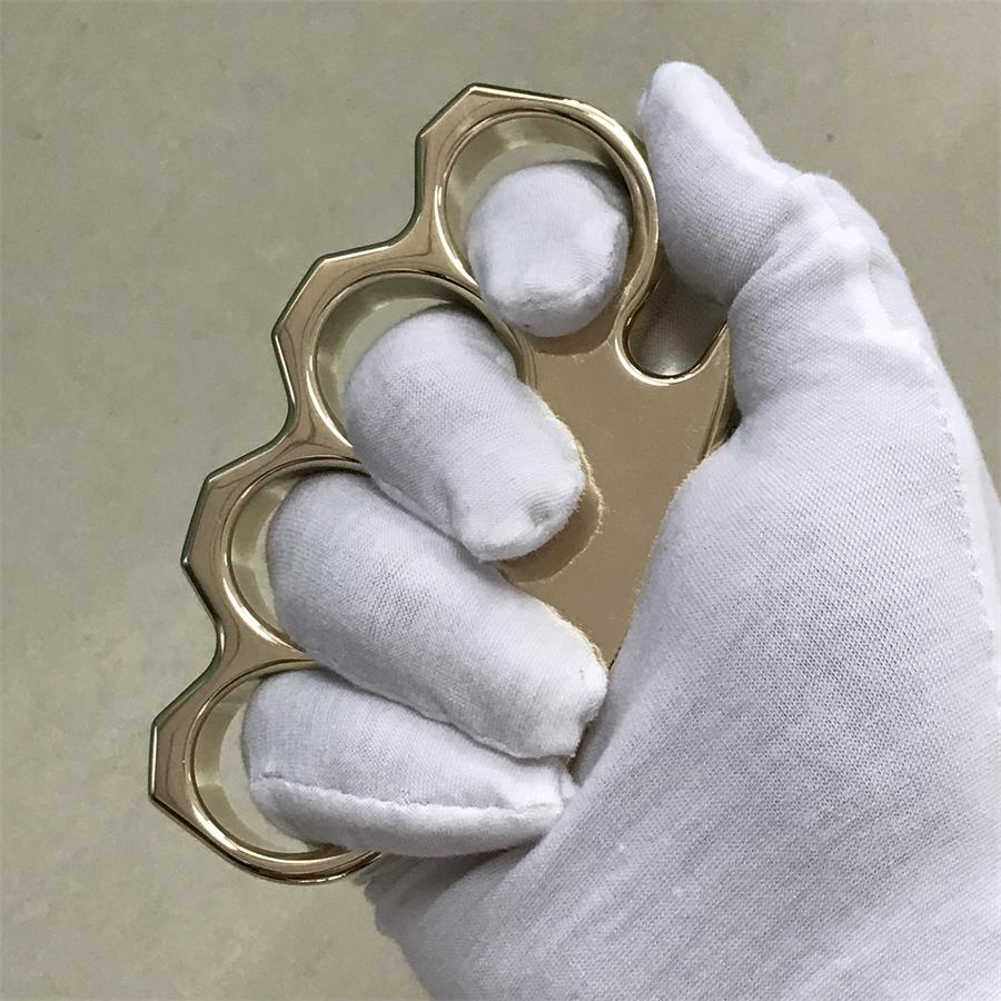 Brass knuckle duster held upright in a white gloved hand with the pointed ends facing up and down