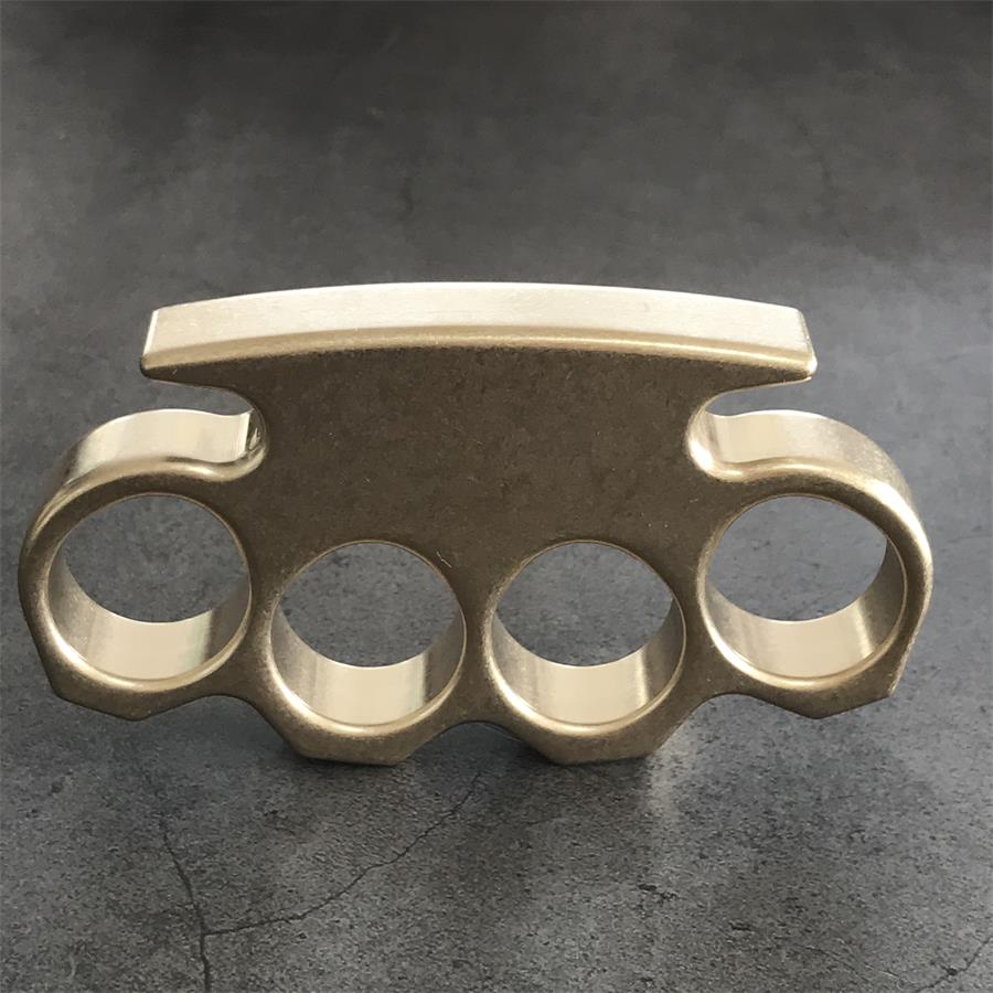 Brass knuckle duster standing upright on dark stone, displaying the top strike bar and four rings.