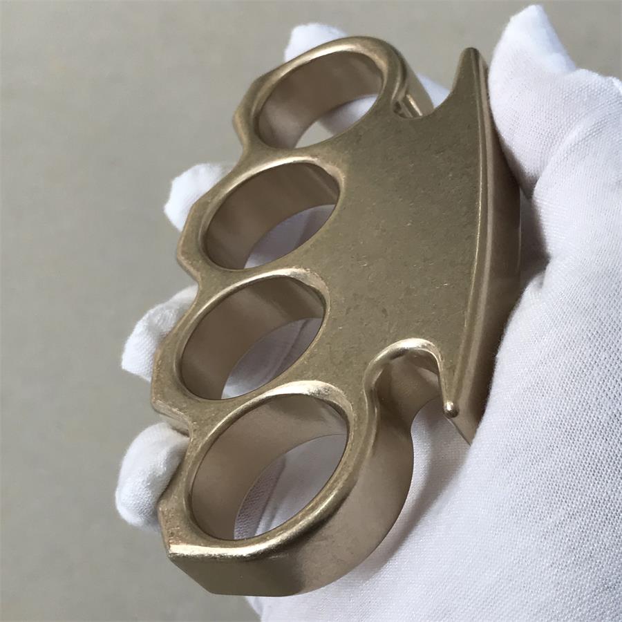 Tilted side view of the brass knuckle duster held in a gloved hand.