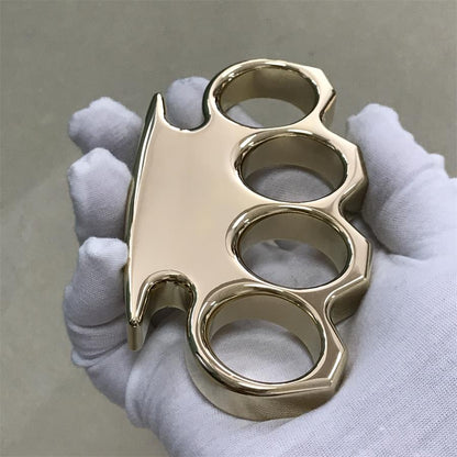 Brass knuckle duster viewed from the side with the wide top bar and stepped finger holes in a gloved hand