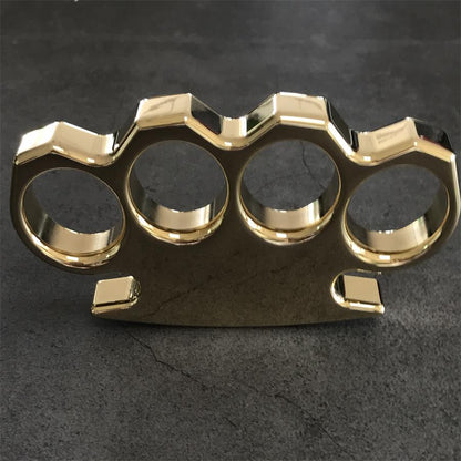 Brass knuckle duster standing upright on a grey stone surface with the wavy top edge and square feet