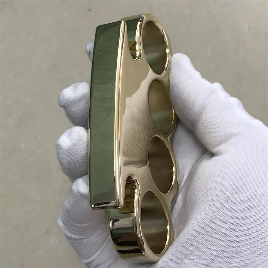 Wide side view of a solid brass knuckle duster showing the smooth flat spine in a gloved hand