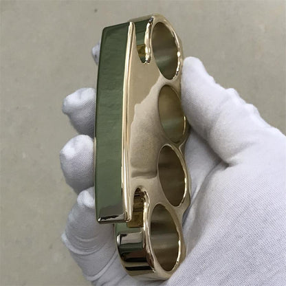 Wide side view of a solid brass knuckle duster showing the smooth flat spine in a gloved hand