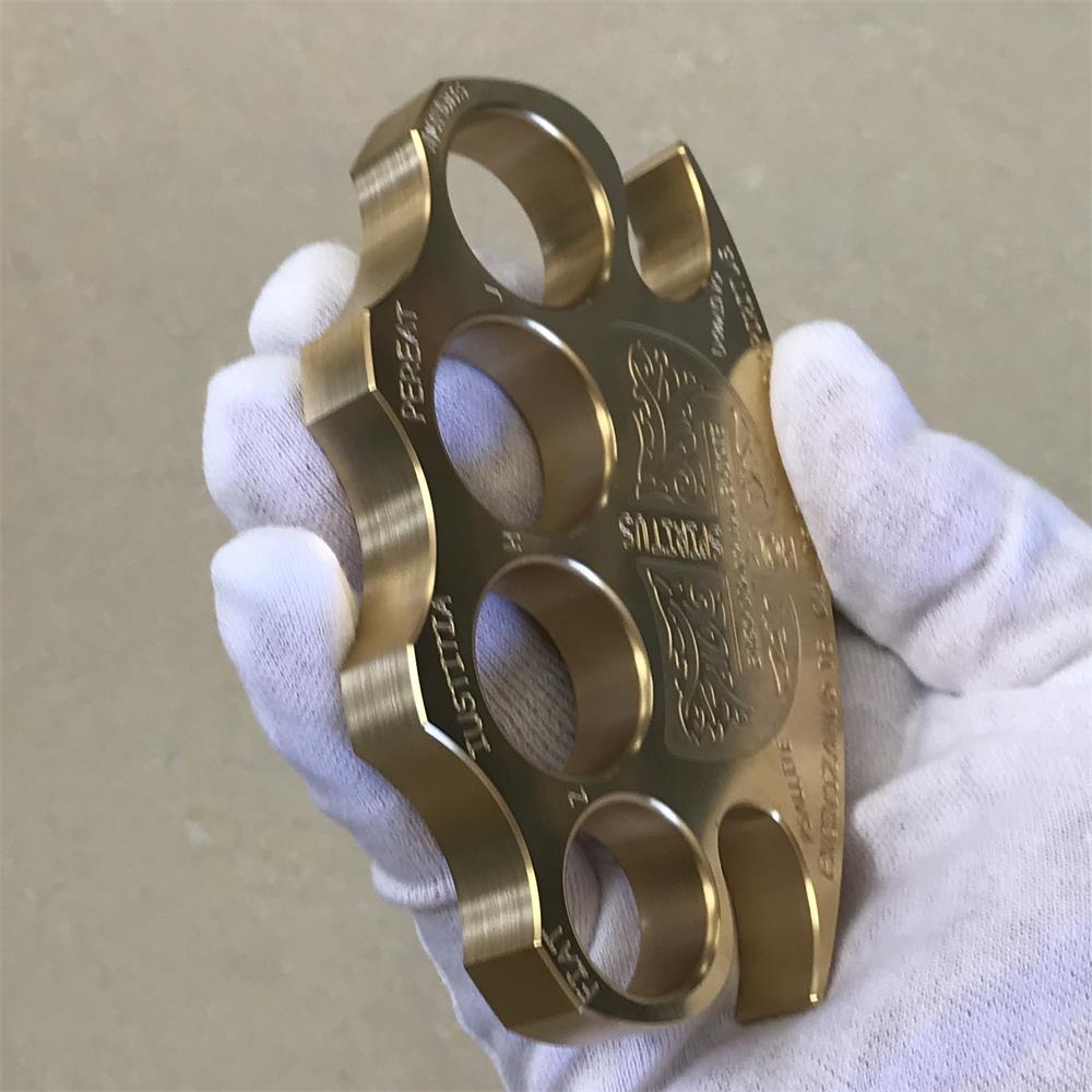 Brass knuckle duster worn across a white gloved hand with the fingers resting through the four holes
