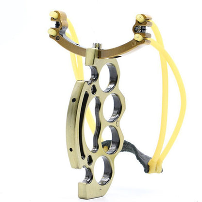 Brass-tone knuckle slingshot standing upright with yellow bands and leather pouch, four finger holes in the grip
