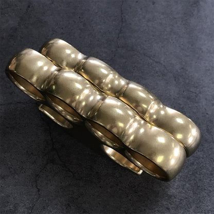 Two brass knuckle dusters lying side by side, rounded outer edges and glossy brass in view