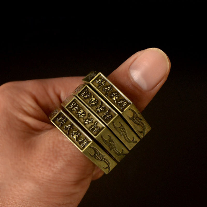 Brass stacked hexagon rings worn on a finger showing engraved characters and flame motifs on each band