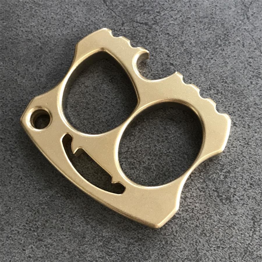 Brass two-hole knuckle flat lay with serrated peaks and smile cutout on grey stone