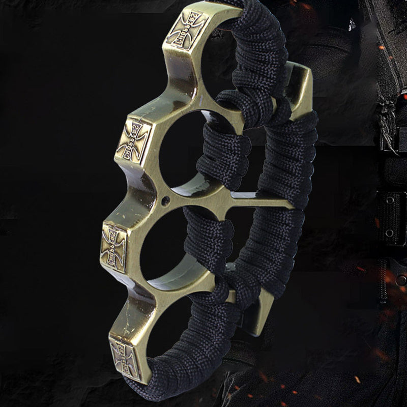 Bronze three-hole knuckle duster with black paracord grip and embossed cross emblems on dark background