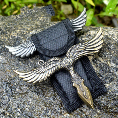 Bronze eagle pendant on a black nylon sheath with a silver gray eagle behind it on a rocky surface