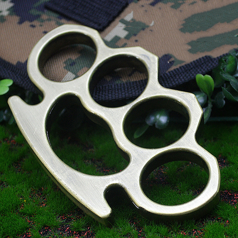 Bronze-H aluminum knuckle duster on camouflage fabric and grass close-up, alternate view