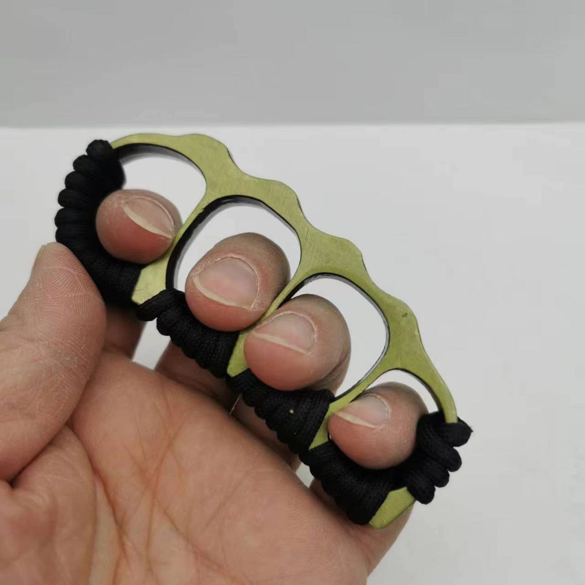 Bronze knuckle duster worn across four fingers, black paracord coils along the wavy upper edge