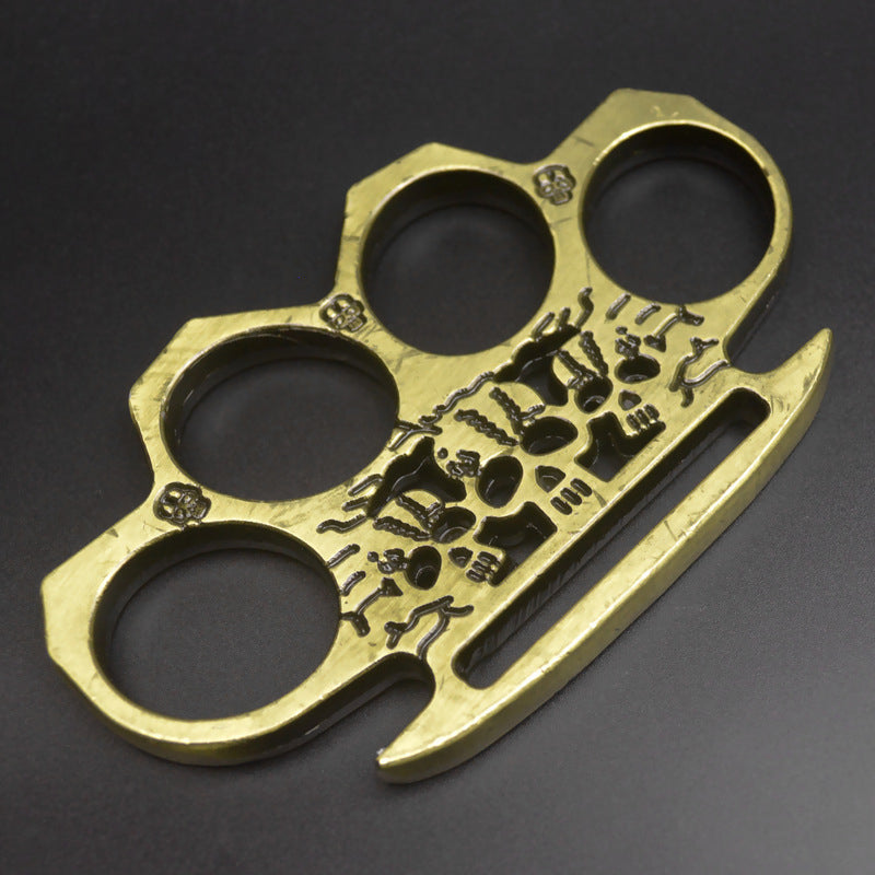 Bronze skeleton knuckle duster lying flat showing the skull artwork and beveled corners along the rim