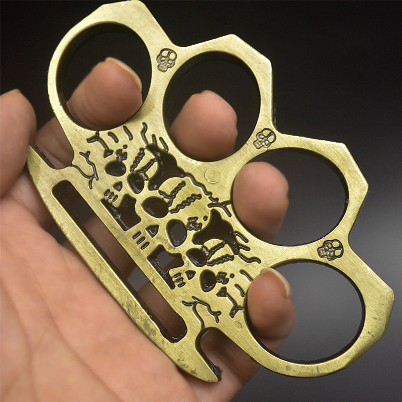 Bronze skeleton knuckle duster held in hand showing the skull engraving and three skull stamps between the holes