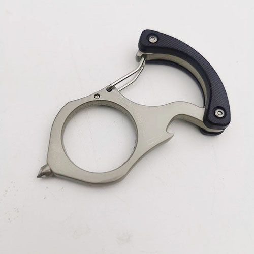 Black handled carabiner keychain tool on a white surface with textured scales, steel spring gate, large round hole and pointed glass breaker tip