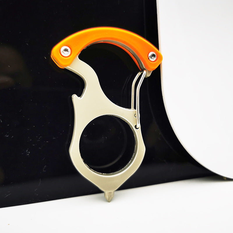 Orange handled carabiner keychain tool clipped onto the edge of a glossy black surface, spring gate open, round finger hole and pointed tip facing down