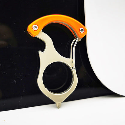 Orange handled carabiner keychain tool clipped onto the edge of a glossy black surface, spring gate open, round finger hole and pointed tip facing down